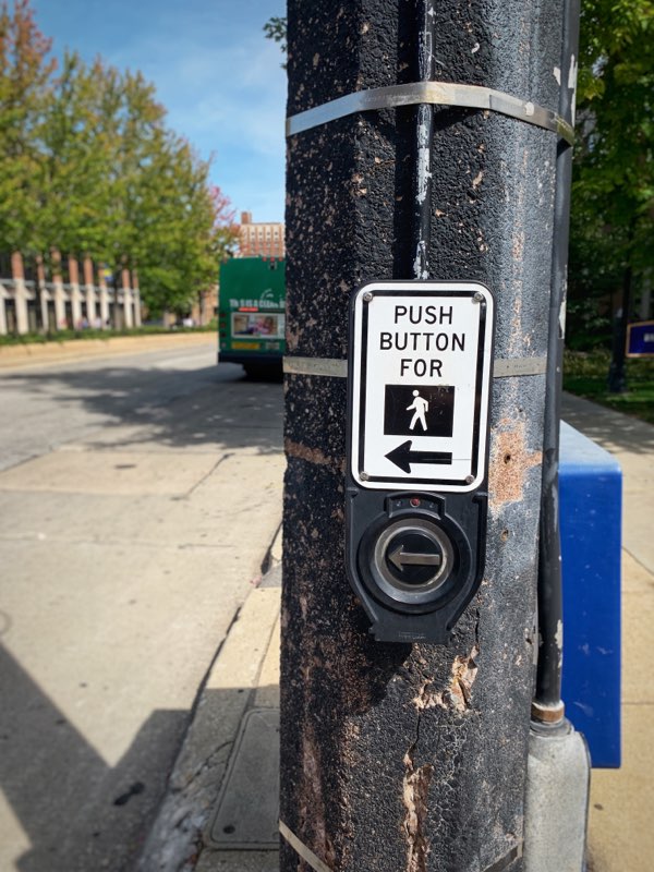 Accessible sidewalk crossing button. Sign reads "Push button for [walk sign image]"